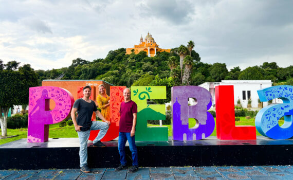 drei Personen vor Schild Puebla und Berg im Hintergrund